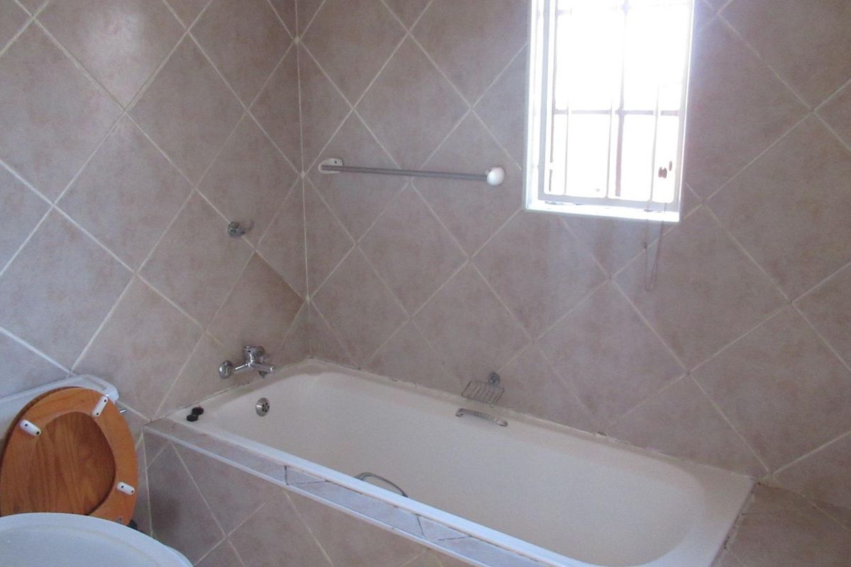 A functional bathroom featuring a built-in bathtub, tiled walls, and a window with security bars.