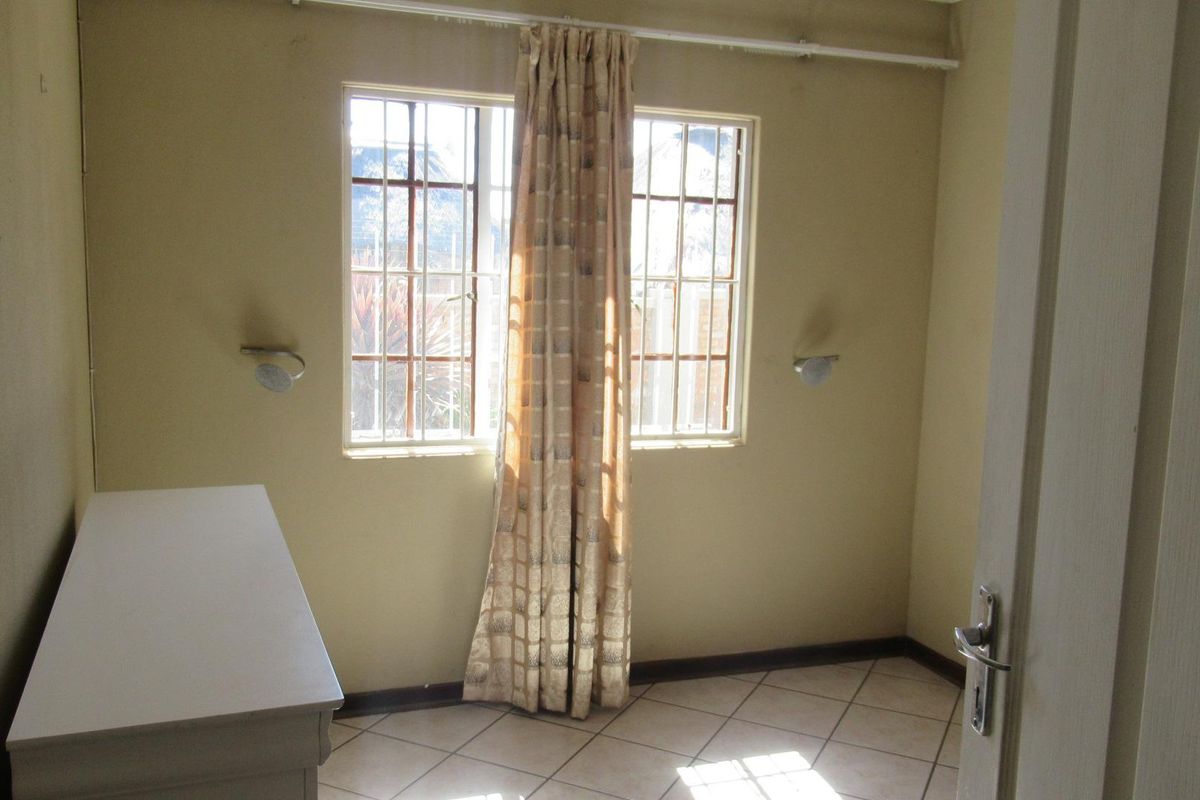 A simple bedroom featuring tiled flooring, security bars on the windows, and wall-mounted lighting fixtures.