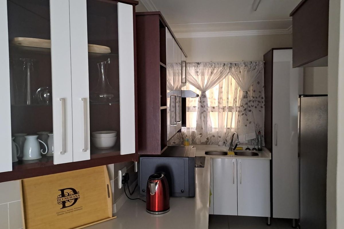 A compact kitchen featuring two-tone cabinetry, a double-basin sink, and integrated storage space, providing a functional layout for daily meal preparation.