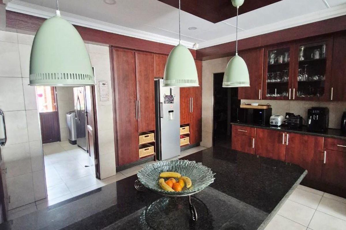Spacious kitchen featuring dark wood cabinetry, a large granite-topped island, pendant lighting, and a dedicated scullery area with tiled flooring.