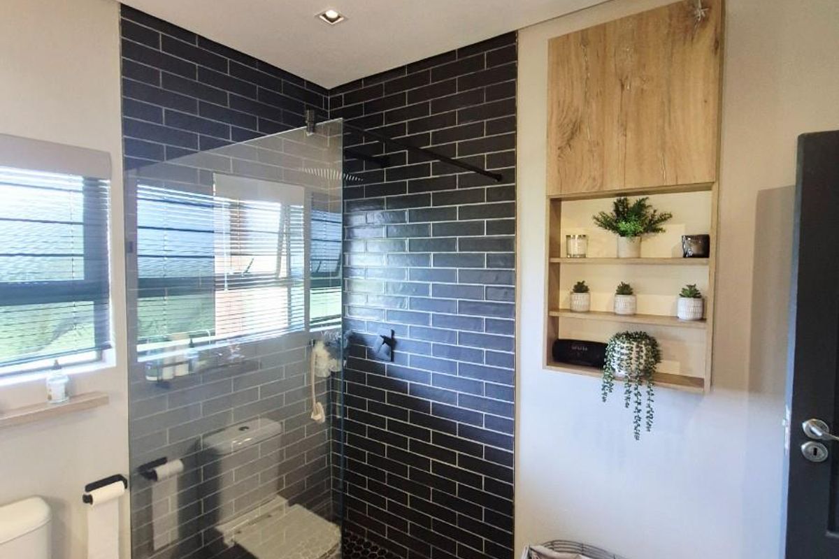 Modern bathroom featuring a walk-in shower with dark subway tiles, hexagonal floor tiles, a glass partition, and built-in wooden shelving.