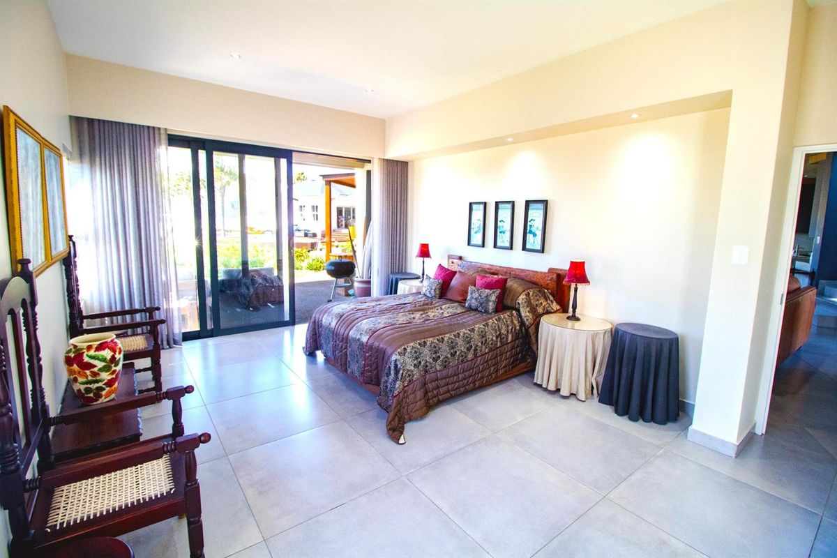 Spacious bedroom featuring large format floor tiles, recessed ceiling lighting, and sliding glass doors providing direct access to the outdoor patio area.