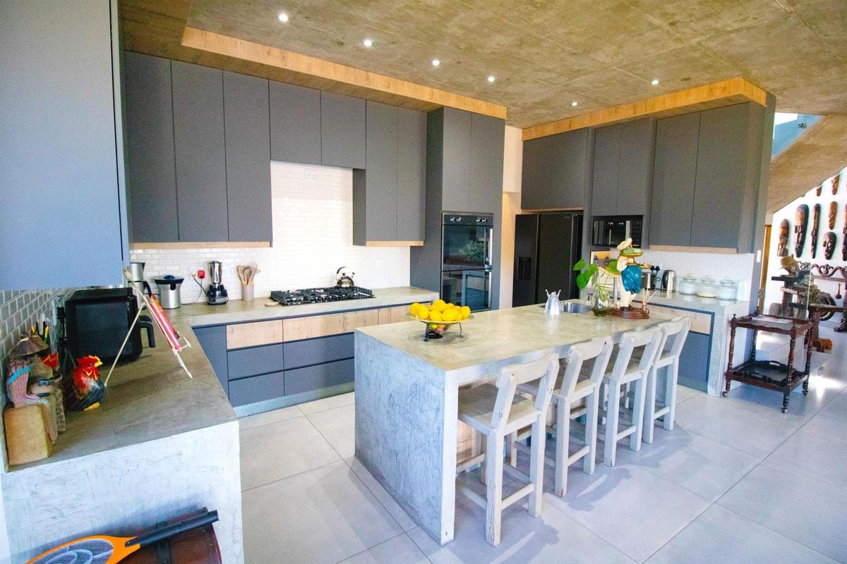 Modern kitchen featuring concrete island, sleek grey cabinetry, built-in oven, gas cooktop, and exposed concrete ceiling with recessed lighting.