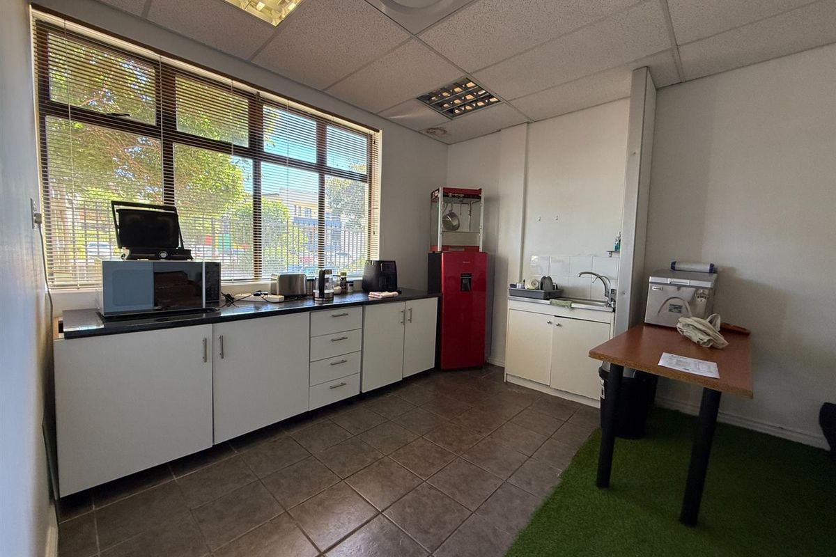 A functional office kitchenette featuring built-in cabinetry, a sink, and large windows providing natural light.