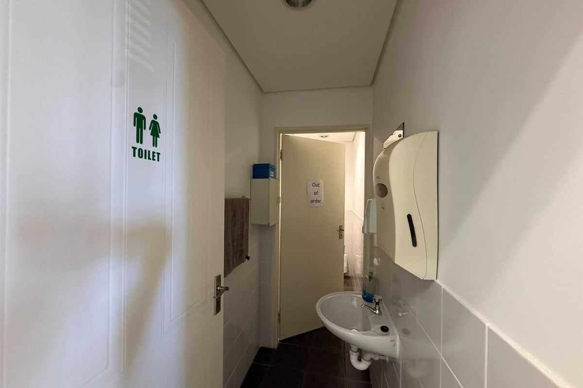 A functional office restroom area featuring a wall-mounted basin, soap dispenser, and tiled flooring.