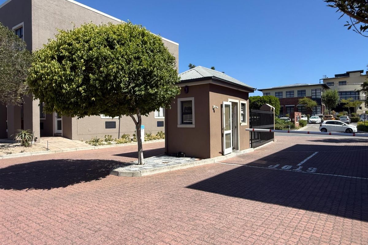 A secure office park entrance featuring a guard house, paved driveway, and automated boom gate access control.