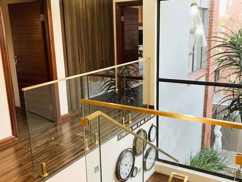 A modern landing area featuring a glass balustrade with brass handrails, timber staircase, built-in cabinetry, and a large window overlooking the exterior.