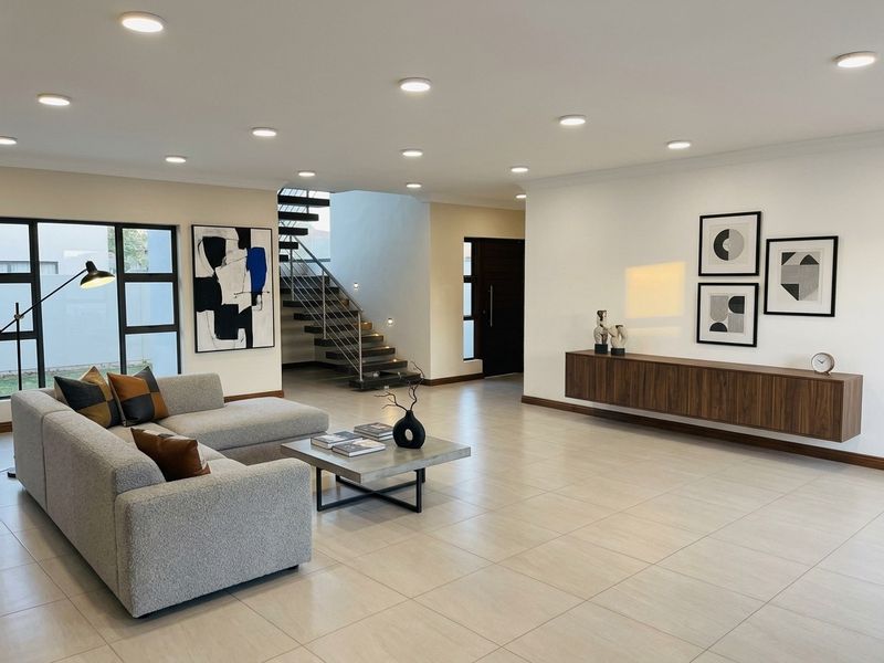 Spacious open-plan living area featuring large format floor tiles, recessed downlights, a modern floating timber cabinet, and a striking staircase with metal balustrade.