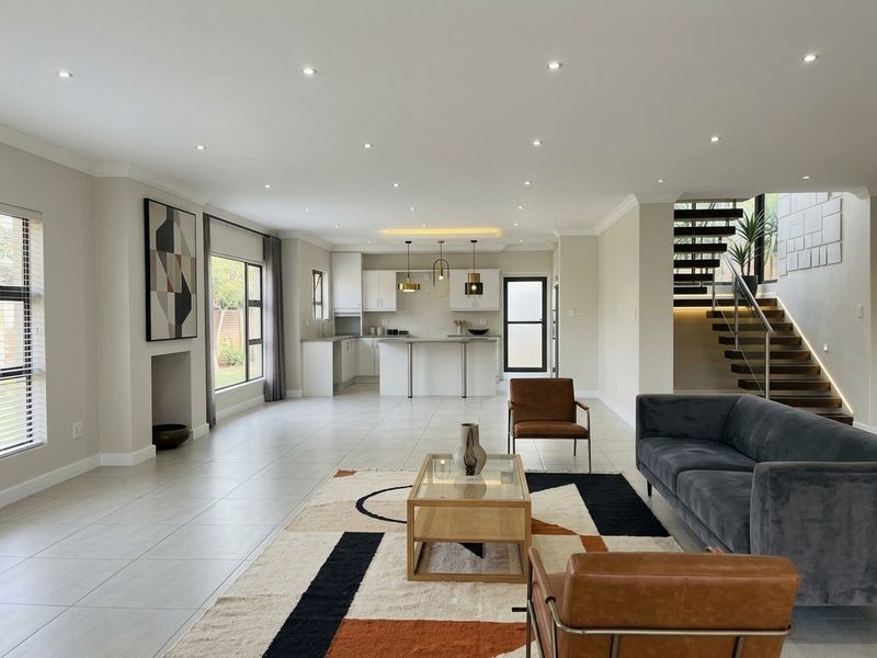 Spacious open-plan living area featuring a modern kitchen with island, tiled floors, recessed lighting, and a contemporary staircase with glass balustrade.