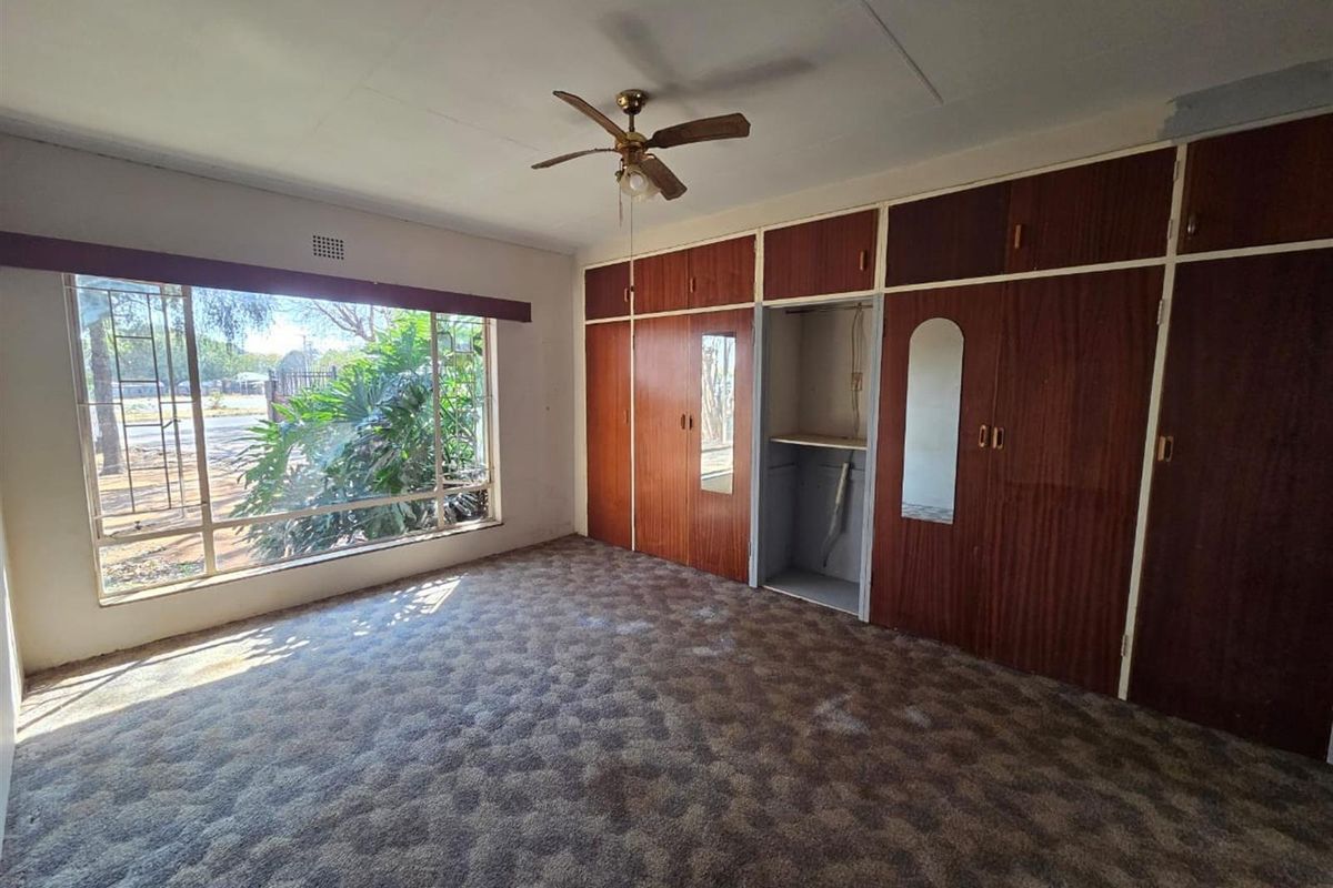 A bedroom featuring built-in wooden cupboards, a ceiling fan, and large windows providing natural light.