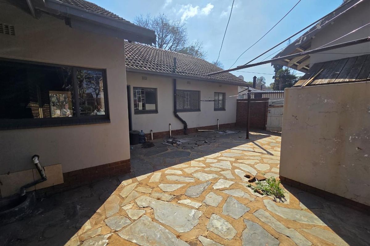 Rear exterior view of the property featuring a paved courtyard area, tiled roof, and exterior wall finishes requiring maintenance.