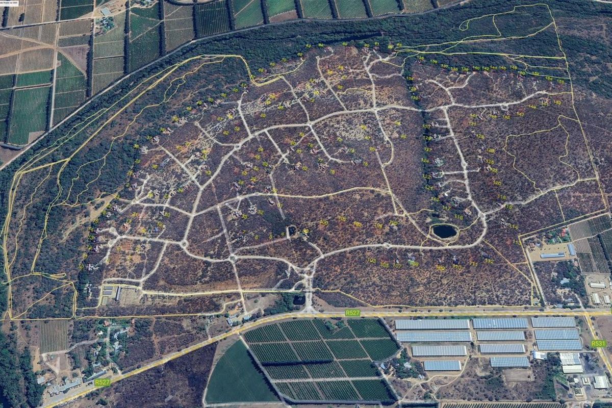 An aerial view of a large residential estate showing the layout of plots, internal road infrastructure, and surrounding natural landscape.
