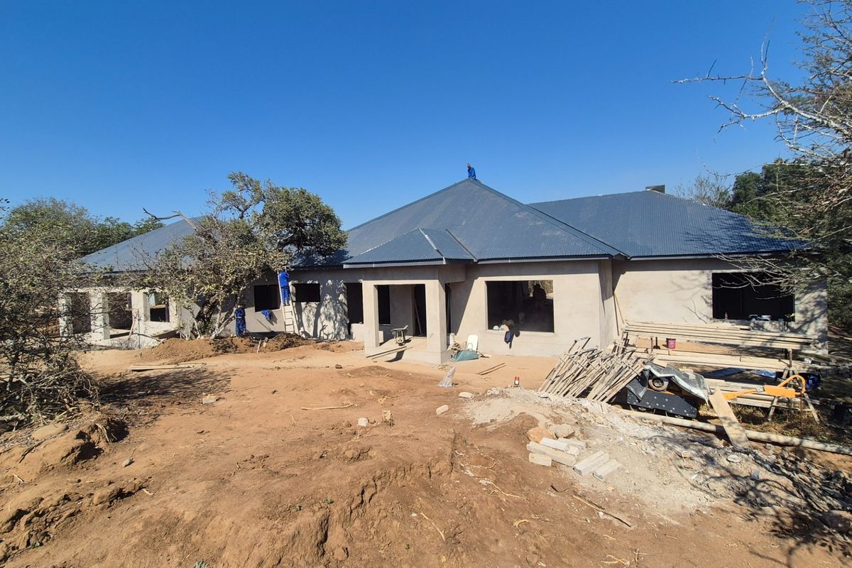 A rear view of a residential property currently under construction, featuring a completed metal roof and unfinished plastered exterior walls.