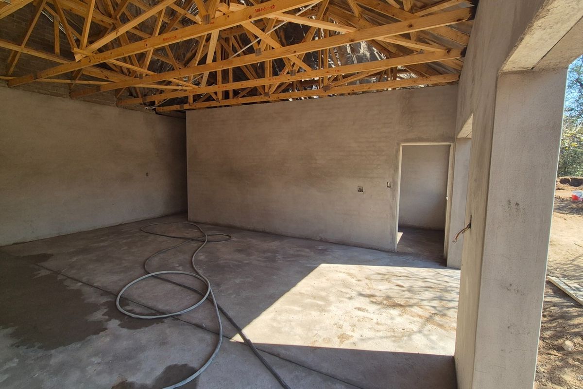 An unfinished interior space featuring exposed timber roof trusses, plastered masonry walls, and cement screed flooring, currently in the construction phase.