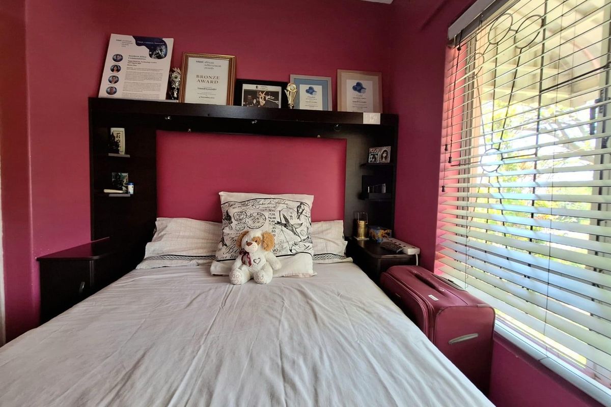 A bedroom featuring a built-in headboard with integrated shelving and a large window with fitted blinds.