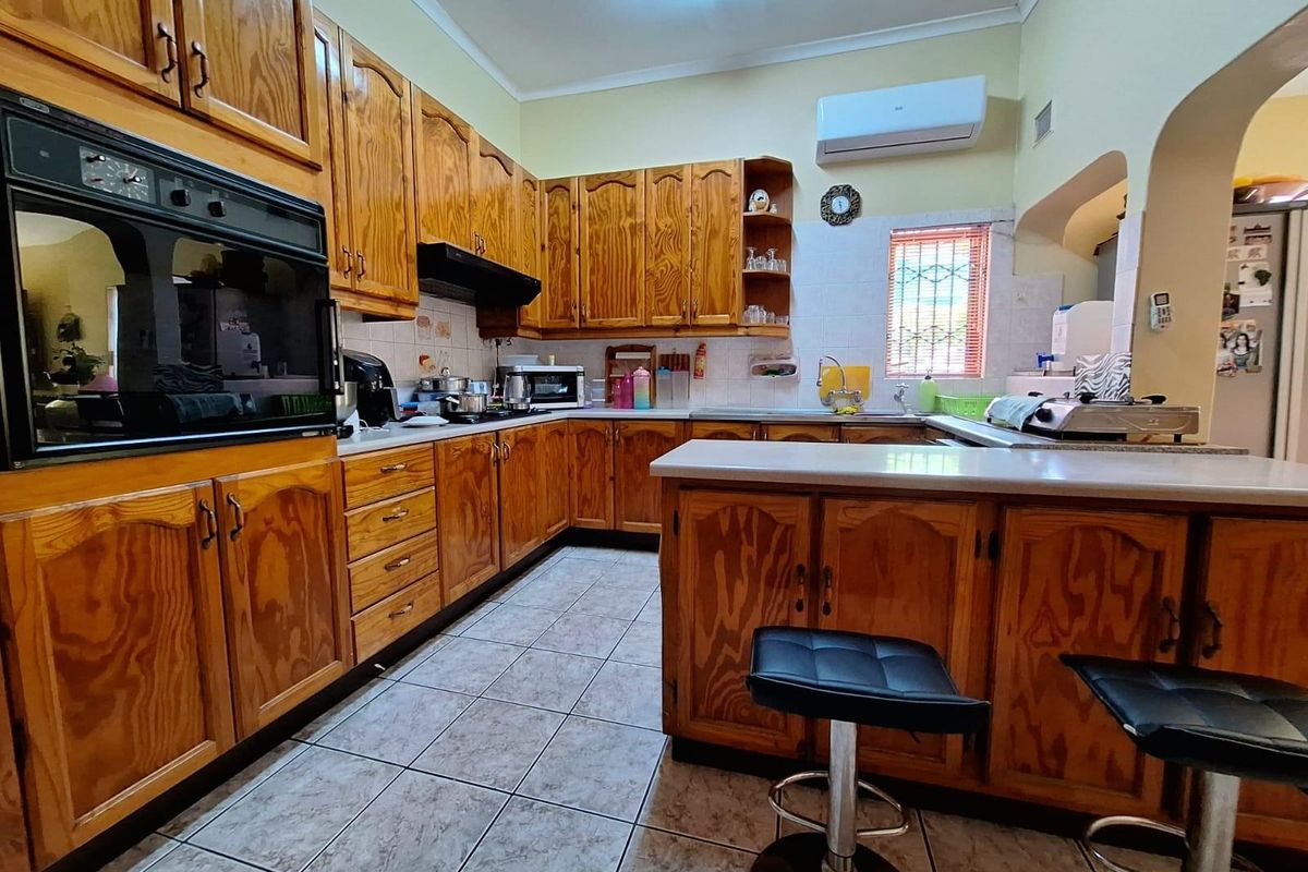 A functional kitchen featuring extensive wooden cabinetry, built-in oven, extractor fan, and a breakfast counter with tiled flooring.