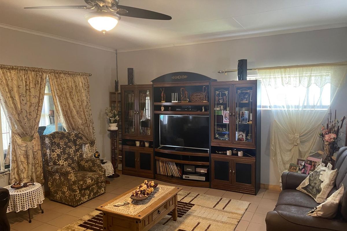 A comfortable living room featuring tiled flooring, a ceiling fan, and large windows that provide natural light.