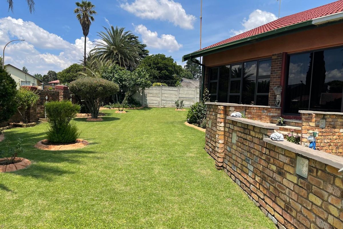 A spacious rear garden featuring a well-maintained lawn, established landscaping, and a brick-built patio area adjacent to the house.
