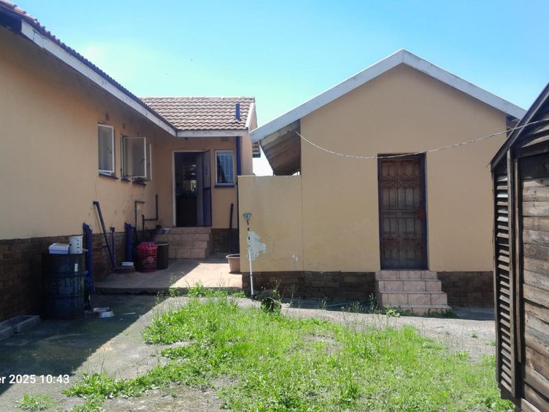 Rear view of the property showing the exterior brick facade, tiled roof, and concrete patio area with access steps.
