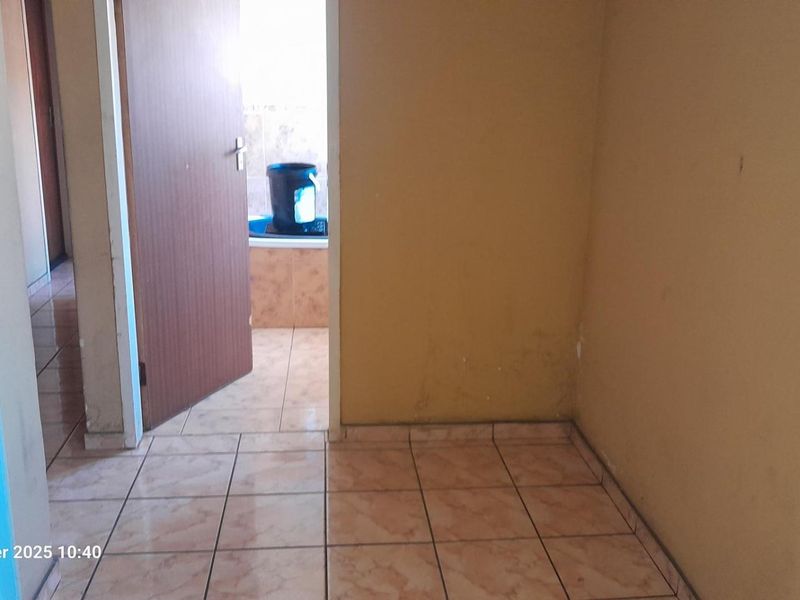 A view of a hallway with tiled flooring leading towards a bathroom area, showing signs of wear on the wall surfaces.