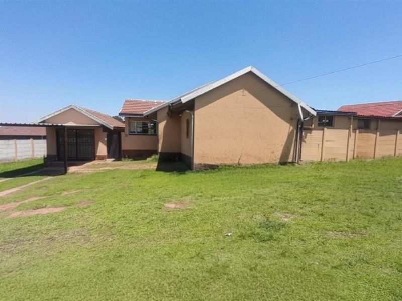 Rear view of the property featuring a large lawn, a carport, and perimeter precast concrete boundary walls.