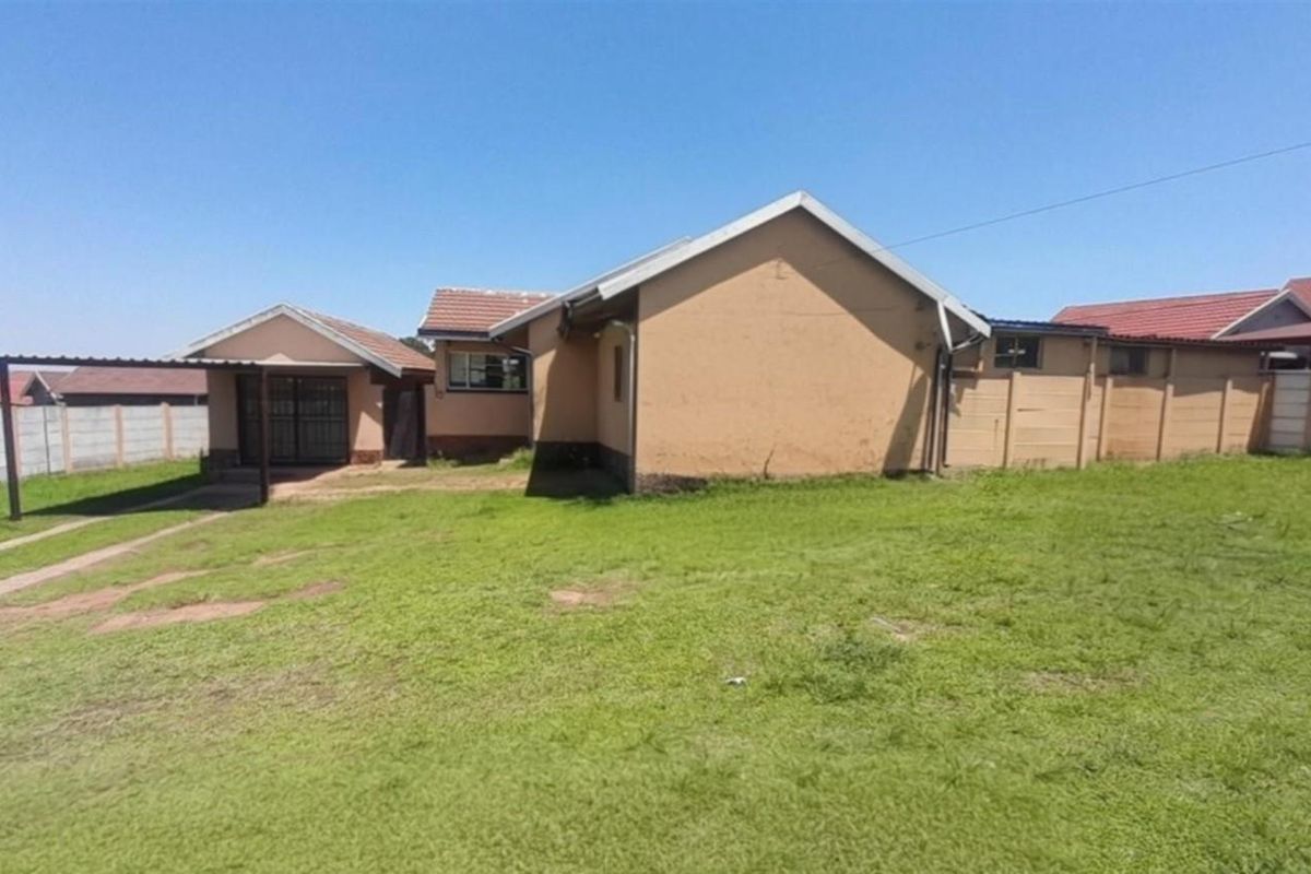 Rear view of the property featuring a large lawn, a carport, and perimeter precast concrete boundary walls.