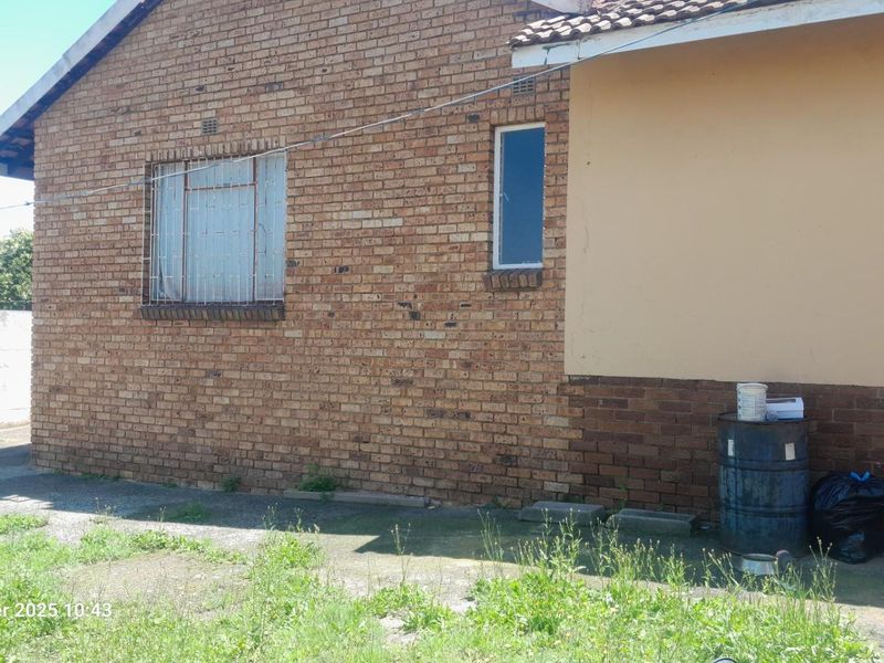 Rear exterior view of the house featuring face brick walls, security bars on windows, and a concrete apron area requiring maintenance.