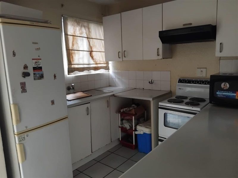 A compact kitchen featuring white cabinetry, a built-in extractor fan, tiled splashbacks, and tiled flooring, offering a functional layout for renovation.
