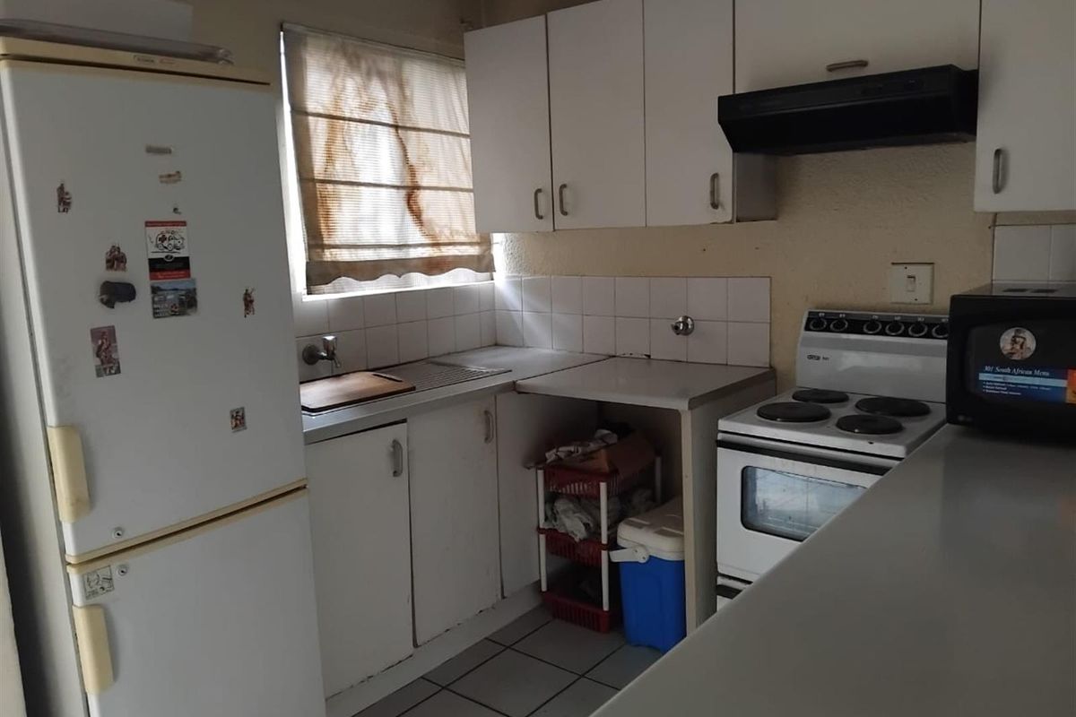 A compact kitchen featuring white cabinetry, a built-in extractor fan, tiled splashbacks, and tiled flooring, offering a functional layout for renovation.