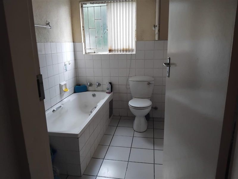 A functional bathroom featuring a built-in bathtub, toilet, and tiled walls and flooring, requiring cosmetic updates to modernize the space.