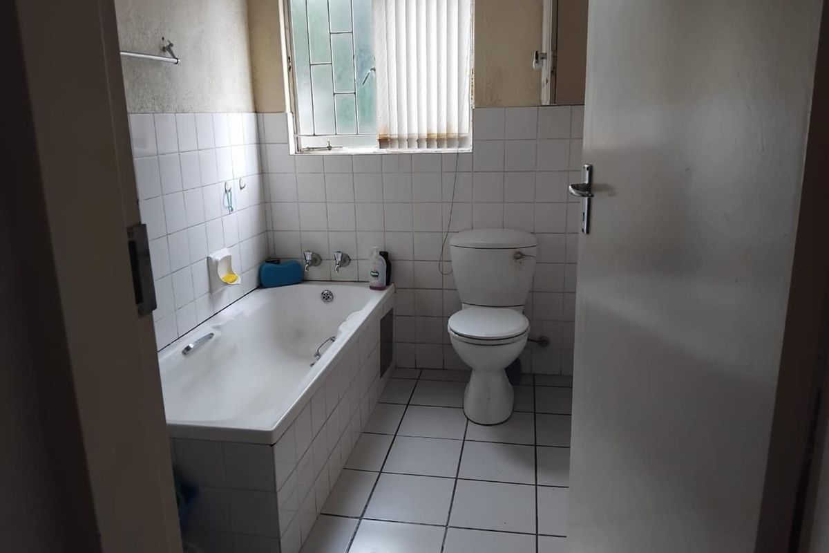 A functional bathroom featuring a built-in bathtub, toilet, and tiled walls and flooring, requiring cosmetic updates to modernize the space.