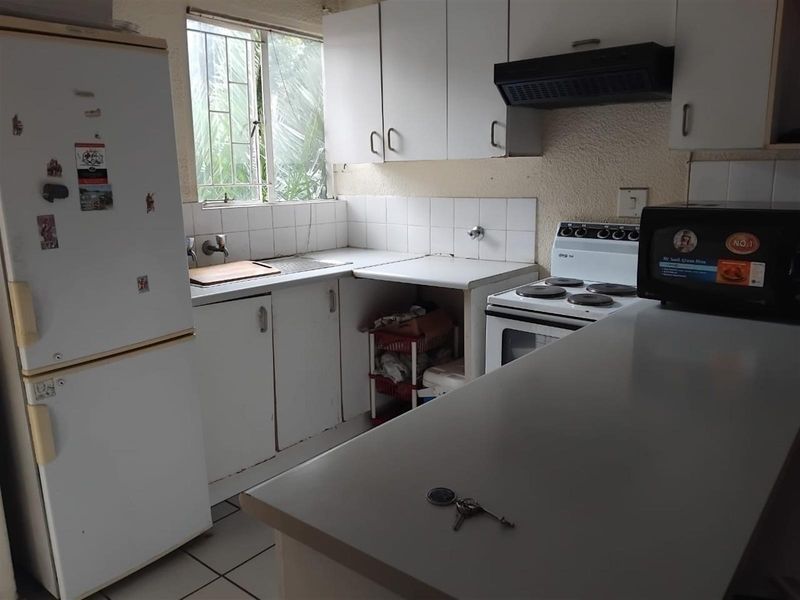 A compact, functional kitchen featuring white cabinetry, a built-in stove with extractor fan, and tiled flooring, offering potential for modernization.
