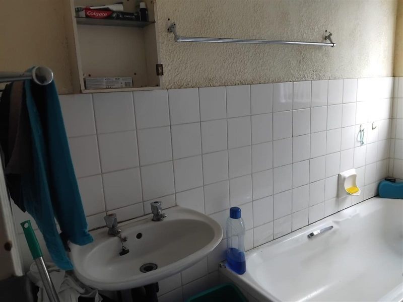 A dated bathroom featuring a standard white bathtub, wall-mounted basin, and tiled splashback with integrated storage shelving.