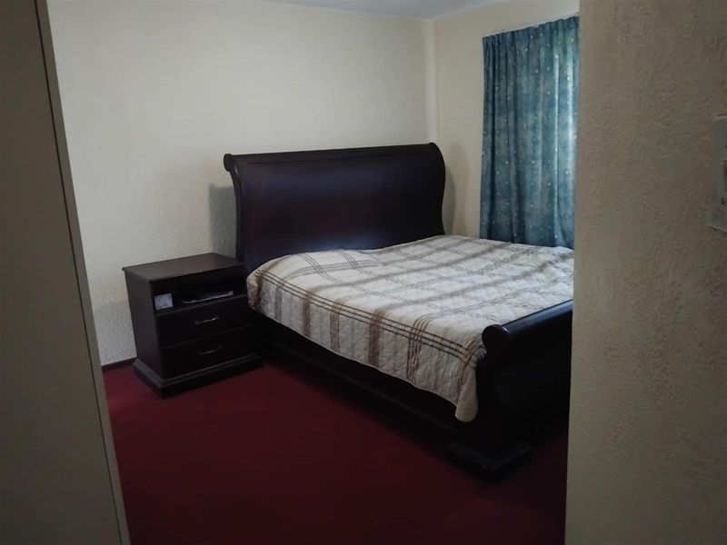 A standard bedroom featuring red carpeting and neutral walls, providing a functional and private sleeping space.