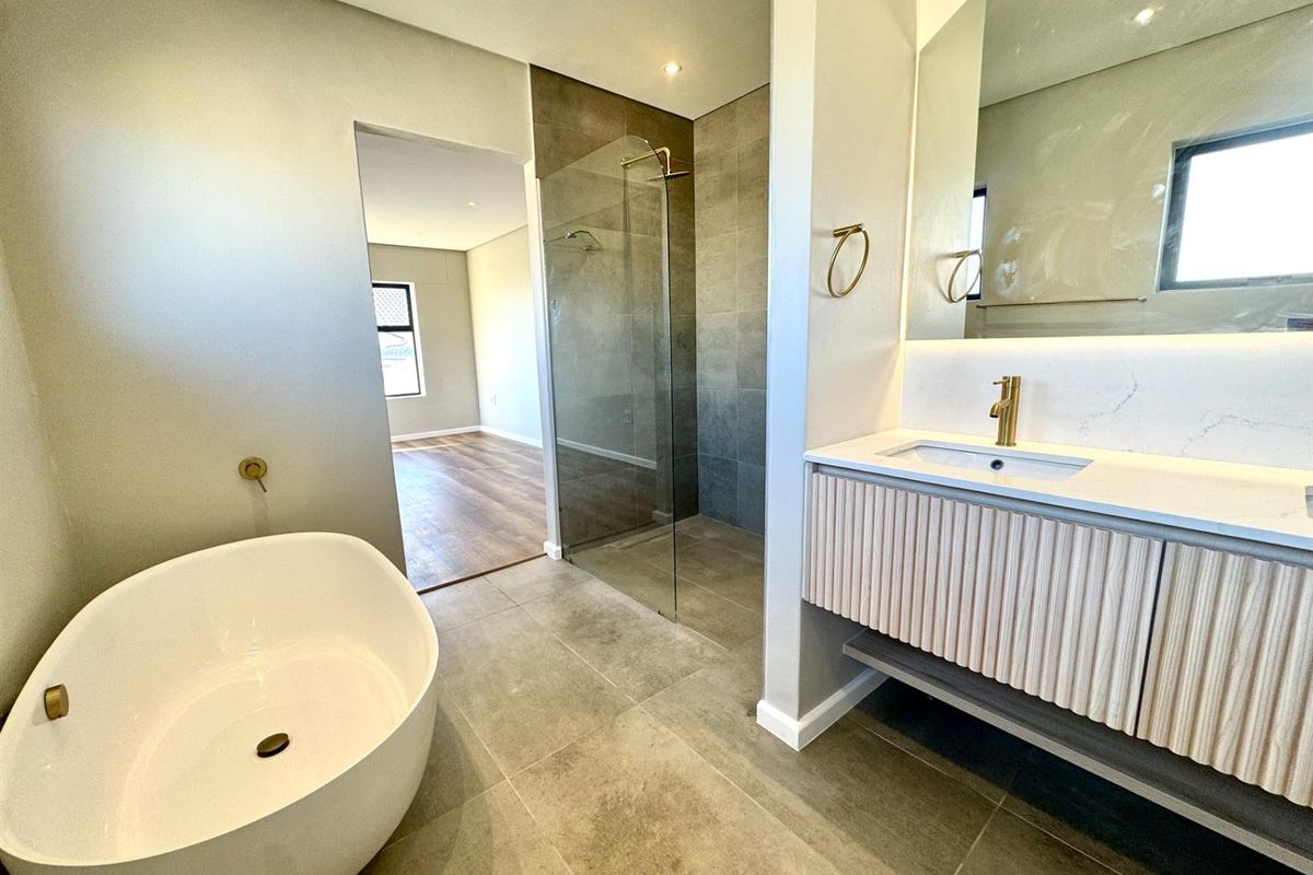 Modern bathroom featuring a freestanding bathtub, walk-in shower with glass screen, and a contemporary wall-mounted vanity with brass fixtures.