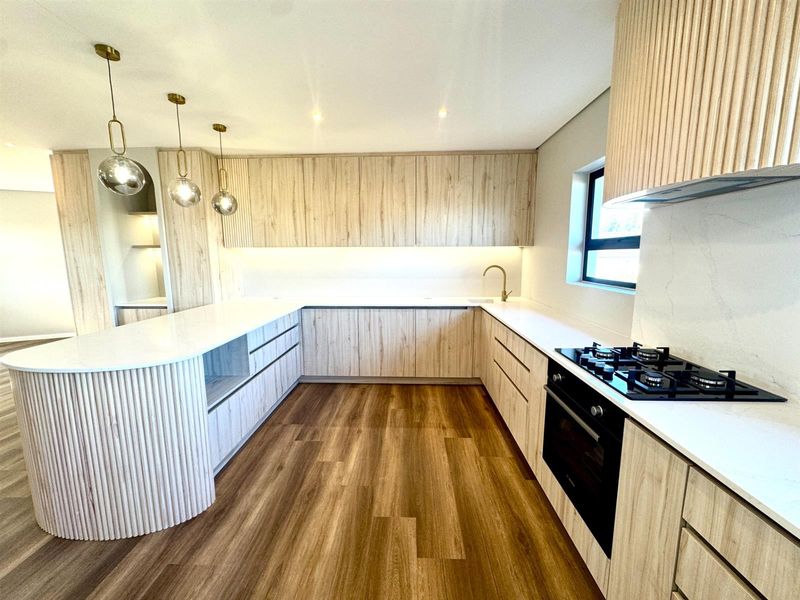 Modern kitchen featuring light wood cabinetry, stone countertops, integrated gas hob, built-in oven, and high-quality finishes throughout.