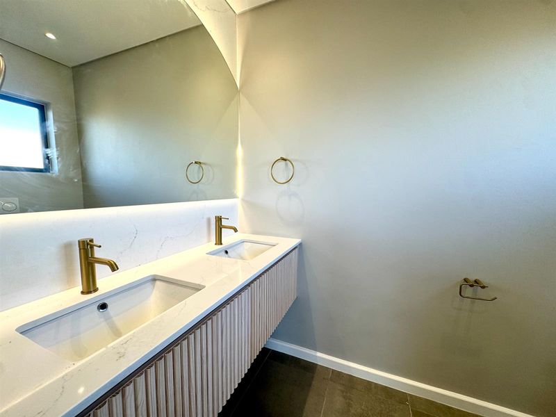 Modern bathroom featuring a double vanity with stone countertop, brass fixtures, large wall mirror, and contemporary fluted cabinetry.