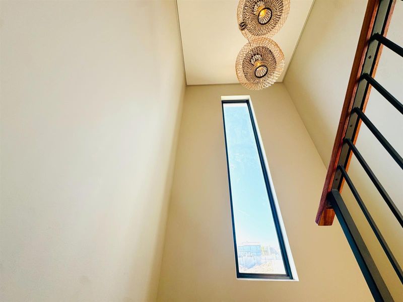 A bright, modern stairwell featuring a tall vertical window, clean neutral walls, and a contemporary staircase with a wooden handrail and metal balustrade.