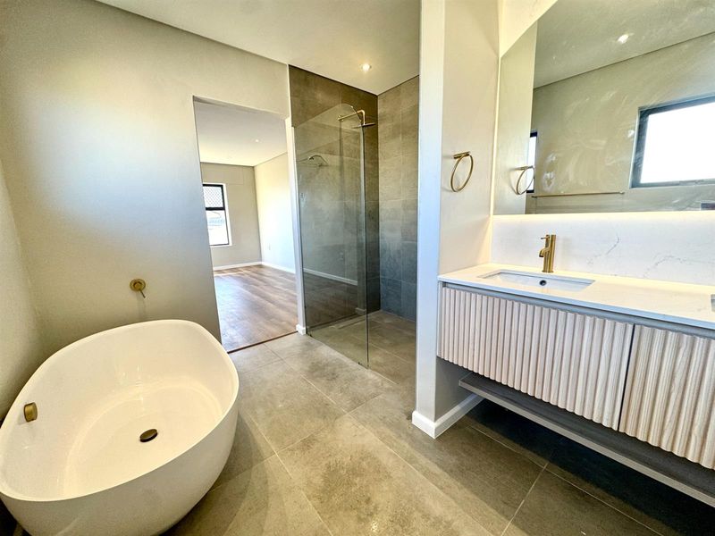 Modern bathroom featuring a freestanding bathtub, walk-in shower with glass screen, and a contemporary wall-mounted vanity with brass fixtures.