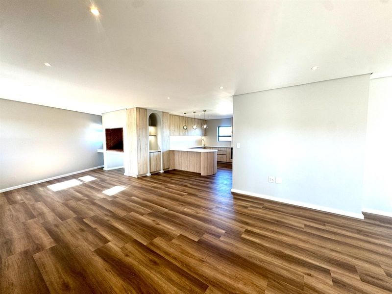 Spacious open-plan living area featuring modern wood-look cabinetry, a kitchen island, and a built-in fireplace with high-quality laminate flooring throughout.