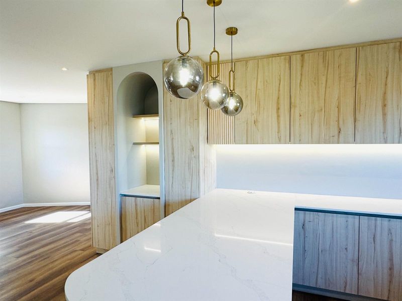 Modern kitchen featuring light wood grain cabinetry, stone countertops, an arched display niche, and elegant pendant lighting in an open-plan layout.