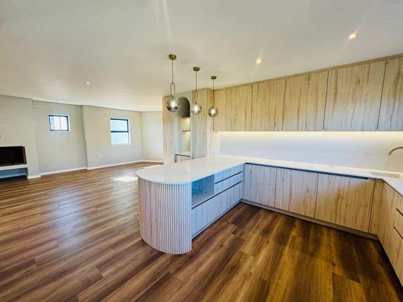 Modern open-plan living area featuring light wood cabinetry, stone countertops, integrated lighting, and a fireplace, creating a seamless and contemporary living space.
