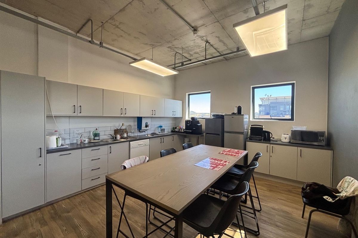 Modern office kitchen featuring light grey cabinetry, laminate countertops, exposed concrete ceilings, and durable laminate flooring, providing a functional break area.