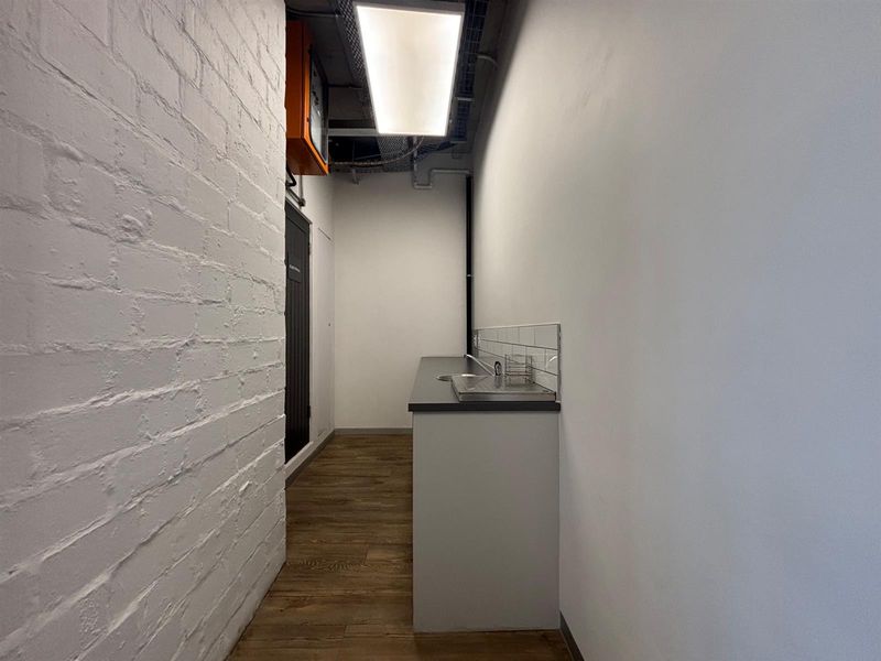 A compact, modern kitchenette or scullery area featuring a stainless steel sink, subway tile backsplash, and durable wood-look flooring in an office setting.