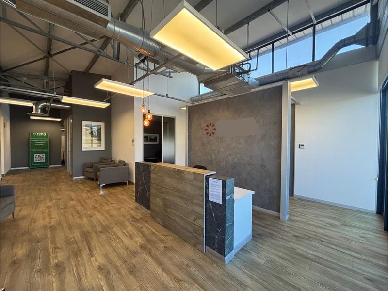 Modern office reception area featuring a contemporary desk, exposed industrial-style ceiling with ductwork, and wood-look flooring.