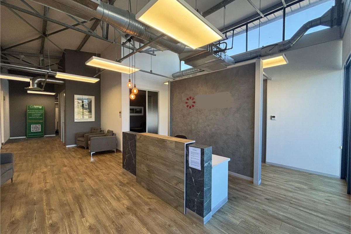 Modern office reception area featuring a contemporary desk, exposed industrial-style ceiling with ductwork, and wood-look flooring.