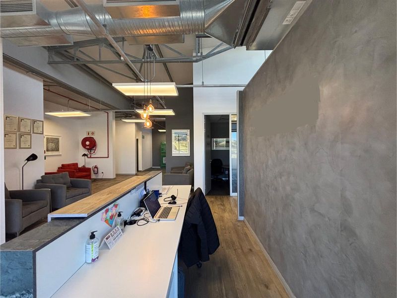 Modern office reception area featuring industrial-style exposed ceilings, a sleek built-in desk, and a contemporary concrete-finish feature wall.