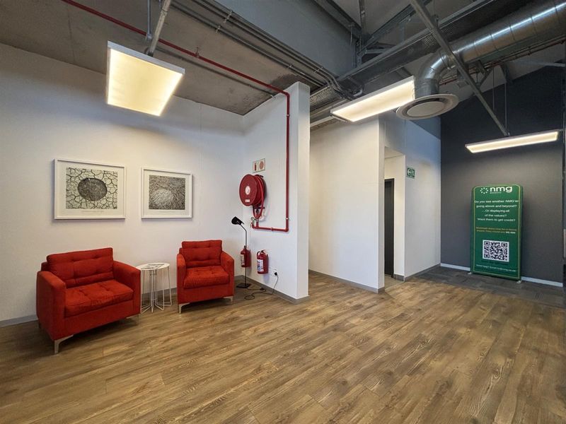 Modern office reception area featuring exposed industrial ceiling, laminate wood flooring, and integrated fire safety equipment.