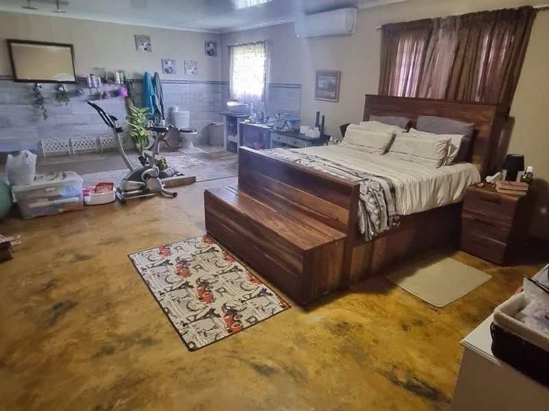 Spacious bedroom featuring polished concrete-style flooring, an integrated en-suite bathroom area, and a wall-mounted air conditioning unit.