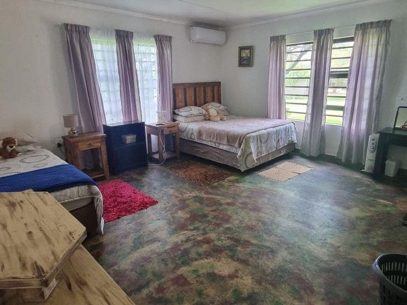 Spacious bedroom featuring large windows for natural light, a wall-mounted air conditioning unit, and unique concrete flooring.